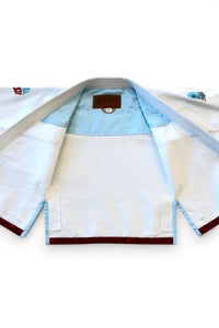 ENIGMA Kimonos white BJJ gi featuring light blue lining, red trim, and tropical embroidery for young athletes.