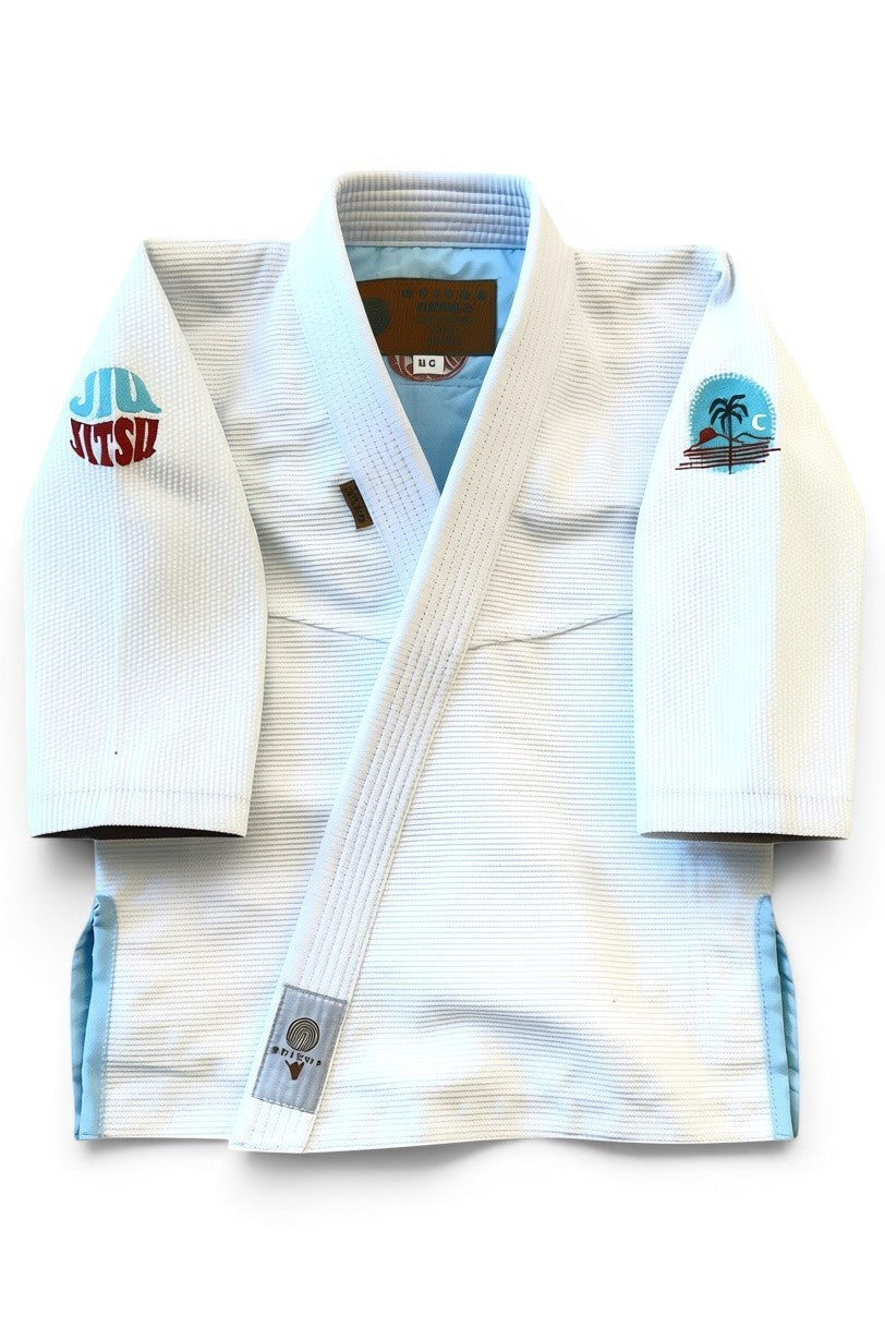 ENIGMA Kimonos white BJJ gi with tropical embroidery, light blue accents, and reinforced stitching for youth athletes.